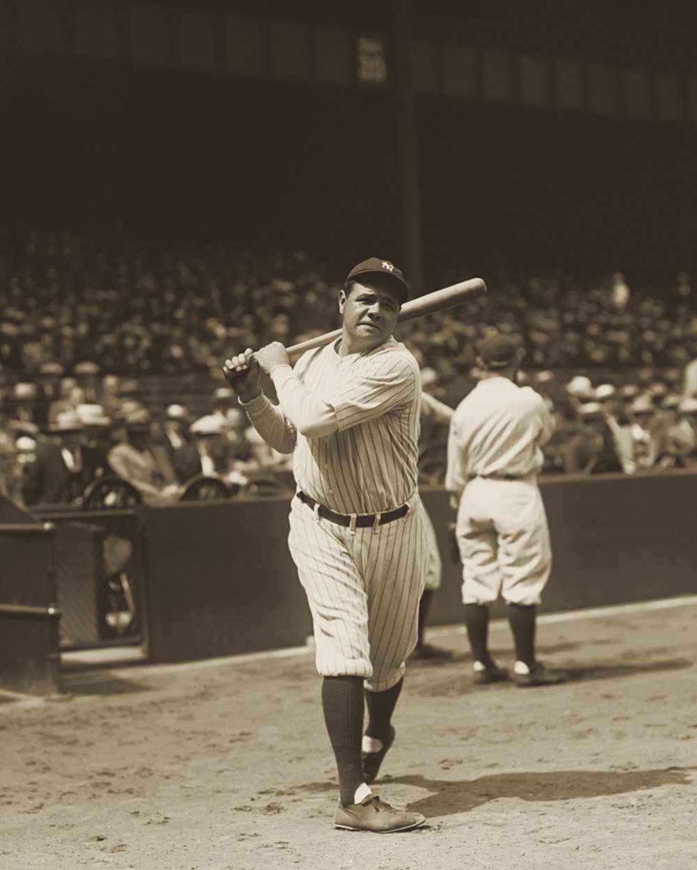Babe Ruth in Yankees pinstripes taking a warm-up swing in front of a crowded grandstand, about 1927.